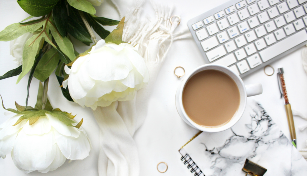 Vue de dessus d'un espace de travail élégant avec un clavier, une tasse de café et des fleurs blanches, illustrant l'authenticité en marketing digital.